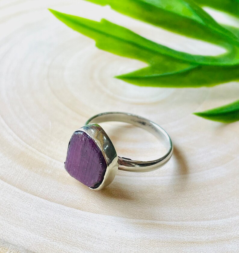 May include: A silver ring with a purple gemstone set in a triangular shape.