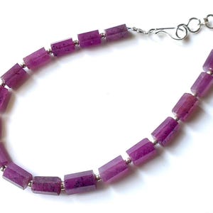 Könnte beinhalten: Eine Halskette aus violetten Edelsteinen mit einem silbernen Verschluss. Die Halskette besteht aus rechteckigen Perlen.