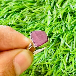 May include: A silver ring with a large, square, purple gemstone. The ring is set on a green background.