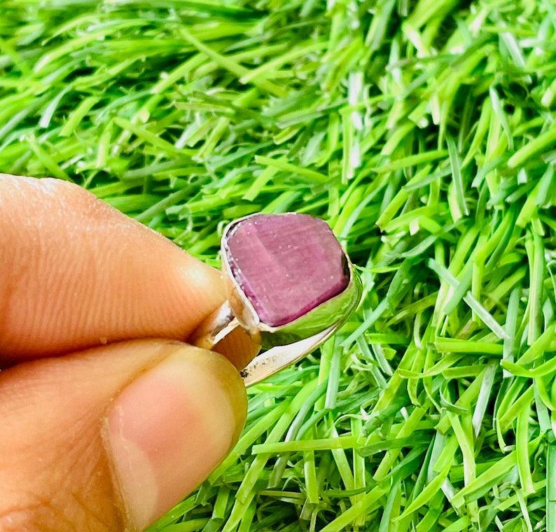 May include: A silver ring with a large, square, purple gemstone. The ring is set on a green background.