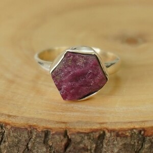 Op de afbeelding: Een zilveren ring met een grote, gefacetteerde, roze robijn-edelsteen gezet in een bezel-setting.