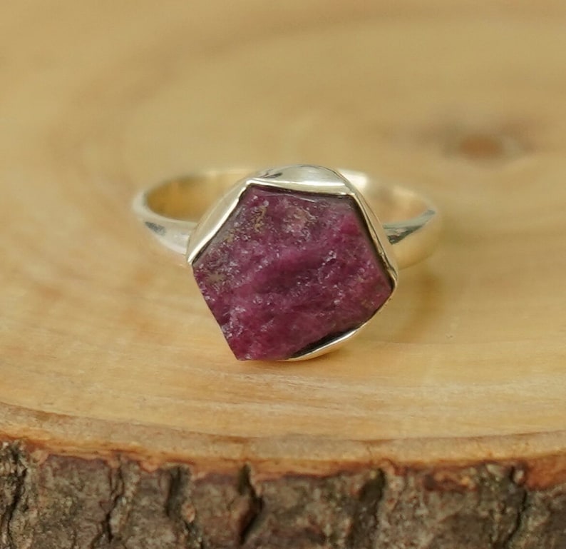 Op de afbeelding: Een zilveren ring met een grote, gefacetteerde, roze robijn-edelsteen gezet in een bezel-setting.