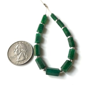May include: A strand of faceted, emerald green gemstone beads with silver-colored spacers. A U.S. quarter coin is next to the beads for size comparison. The beads are strung on a thin, white cord.