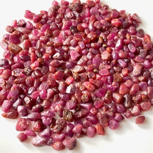 May include: A large pile of small, rough, red ruby gemstones. The rubies are various shades of red and have a natural, unpolished look.