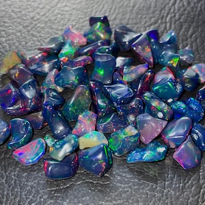 May include: A collection of polished black opal gemstones. The opals display vibrant flashes of color, including green, red, blue, and purple, against a dark background. The gemstones vary in size and shape, showcasing their natural beauty.