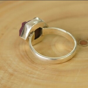 Op de afbeelding: Een zilveren ring met een grote, gefacetteerde, donkerroze edelsteen in een bezel-setting.