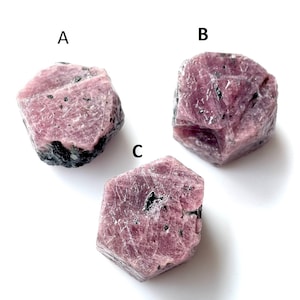 Puede incluir: Tres piedras preciosas de rubí en bruto, de color rojo rosado con inclusiones oscuras. Las piedras están etiquetadas A, B y C. Las piedras tienen un aspecto natural y sin pulir.