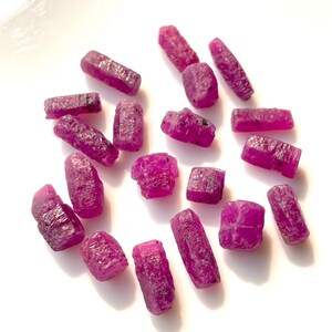 Puede incluir: Una colección de piedras preciosas de rubí rosa en bruto. Las piedras en bruto sin cortar son de varios tamaños y formas, con un color rosa intenso y rico.