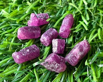 Può includere: Una collezione di sette piccole pietre preziose viola grezze su uno sfondo di erba artificiale verde.