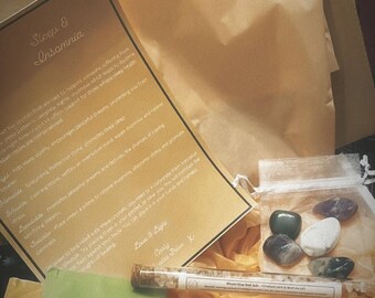 May include: A box filled with items for sleep and insomnia relief. The box contains a small bag of crystals, a tube of peppermint bath salts, and a tea bag. The box also includes a card with information about the crystals and their benefits for sleep.