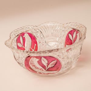 Könnte beinhalten: Eine transparente Glasschale mit dekorativem, gewelltem Rand. Die Schale hat ein geschliffenes Muster und rote ovale Akzente mit weißen Vogel- und Blattmotiven. Ein Vintage-Stück zum Servieren oder Ausstellen.