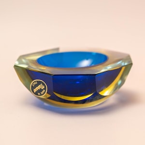 Könnte beinhalten: Ein facettierter Murano-Glas-Behälter in Blau und Gold. Der Behälter hat eine tiefblaue Innenseite und eine transparente Außenseite mit goldenen Akzenten. Ein Aufkleber zeigt "Murano Italy, Made in Italy".
