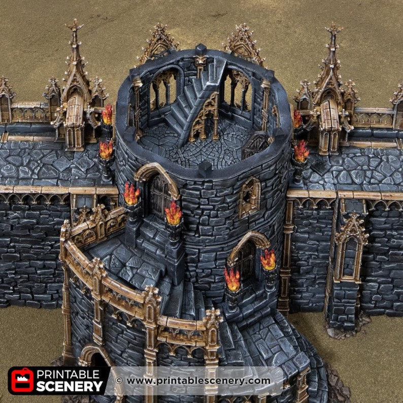 May include: A miniature stone castle tower and wall section featuring dark grey masonry, gold-toned architectural trim, and painted orange flames on wall-mounted torches. The structure includes a central circular tower with stairs.