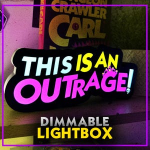 May include: A black, dimmable lightbox with the phrase "THIS IS AN OUTRAGE!" in white, yellow, and pink. The design includes a crown and a skull. The text "DIMMABLE LIGHTBOX" is below the main text.