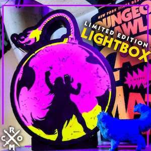 May include: A limited edition lightbox with a neon pink and yellow design featuring a silhouette of a figure. The text "LIMITED EDITION LIGHTBOX" is displayed. A blue dog figurine is in the foreground.