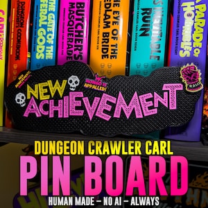 May include: A black, cloud-shaped pin board featuring the text NEW ACHIEVEMENT in bright pink lettering. The board includes small white skull icons, a small Mongo Is Appalled graphic, and a pink fist pin attached to the upper right corner.