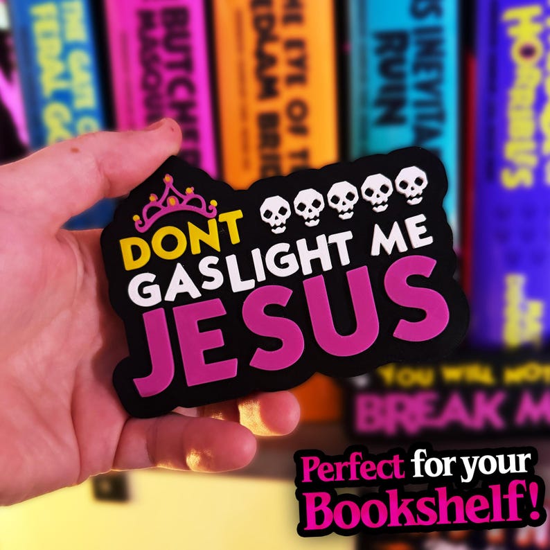 May include: A black die-cut sticker featuring a pink tiara icon, five white skull icons, and the yellow and pink text that reads DONT GASLIGHT ME JESUS. The sticker has a bold, irregular shape and a matte finish with high-contrast lettering.