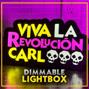 May include: Black, dimmable lightbox with the words "VIVA LA REVOLUCION CARL" in yellow, white, and pink. Features three white skull graphics and the text "DIMMABLE LIGHTBOX". The sign is outlined in yellow.
