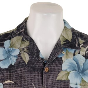 K&ouml;nnte beinhalten: Ein schwarzes Hemd mit Kn&ouml;pfen und einem blauen und gr&uuml;nen Blumenmuster. Das Hemd hat einen Kragen und einen Knopfverschluss.