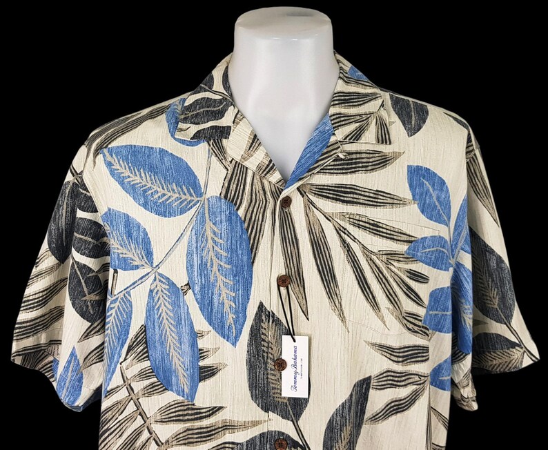 May include: A short-sleeved button-down shirt with a tropical leaf print in shades of blue, black, and beige. The shirt has a white background and a Tommy Bahama label.