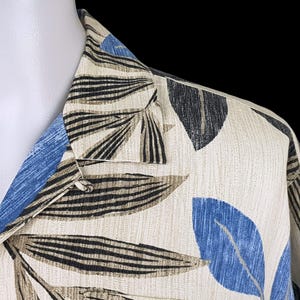 May include: A beige button-up shirt with a tropical leaf print in shades of blue, black, and brown. The shirt has a collar and a button closure.