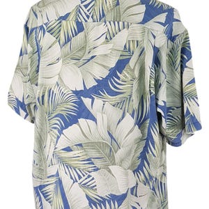 Puede incluir: Una camisa de manga corta con estampado azul y blanco con un dise&ntilde;o de hojas tropicales. La camisa tiene cuello abotonado y un corte holgado.