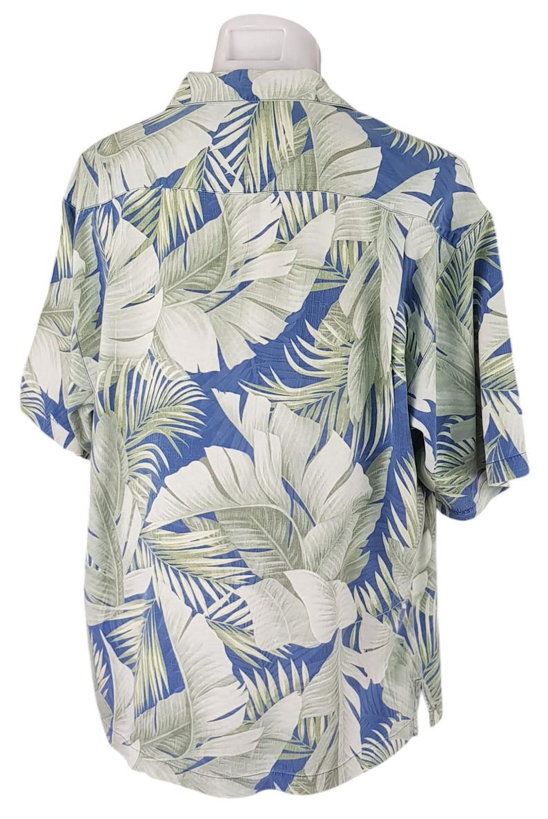 Puede incluir: Una camisa de manga corta con estampado azul y blanco con un dise&ntilde;o de hojas tropicales. La camisa tiene cuello abotonado y un corte holgado.