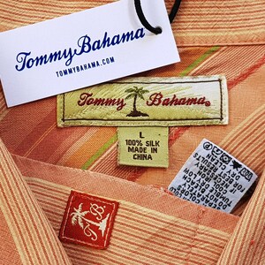 May include: A pink and white striped shirt with a Tommy Bahama label. The label says "100% Silk Made in China".