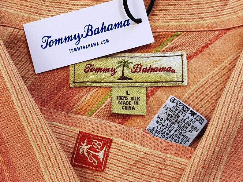 May include: A pink and white striped shirt with a Tommy Bahama label. The label says "100% Silk Made in China".