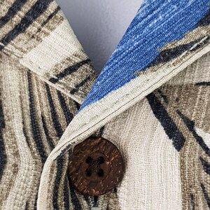 May include: Close-up of a brown wooden button with a cross-shaped design, sewn onto a beige and blue patterned fabric.