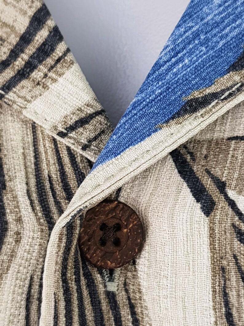 May include: Close-up of a brown wooden button with a cross-shaped design, sewn onto a beige and blue patterned fabric.