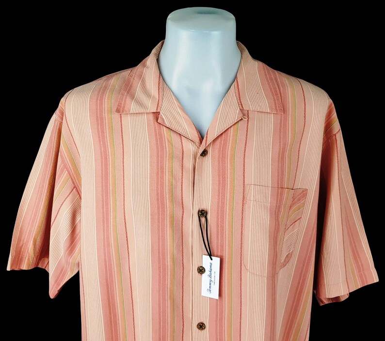 May include: A pink and green striped short-sleeved button-down shirt with a Tommy Bahama label.