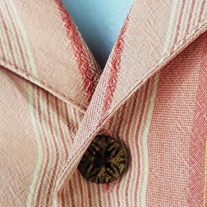 May include: Close-up of a red and white striped shirt with a wooden button. The button has a carved design.