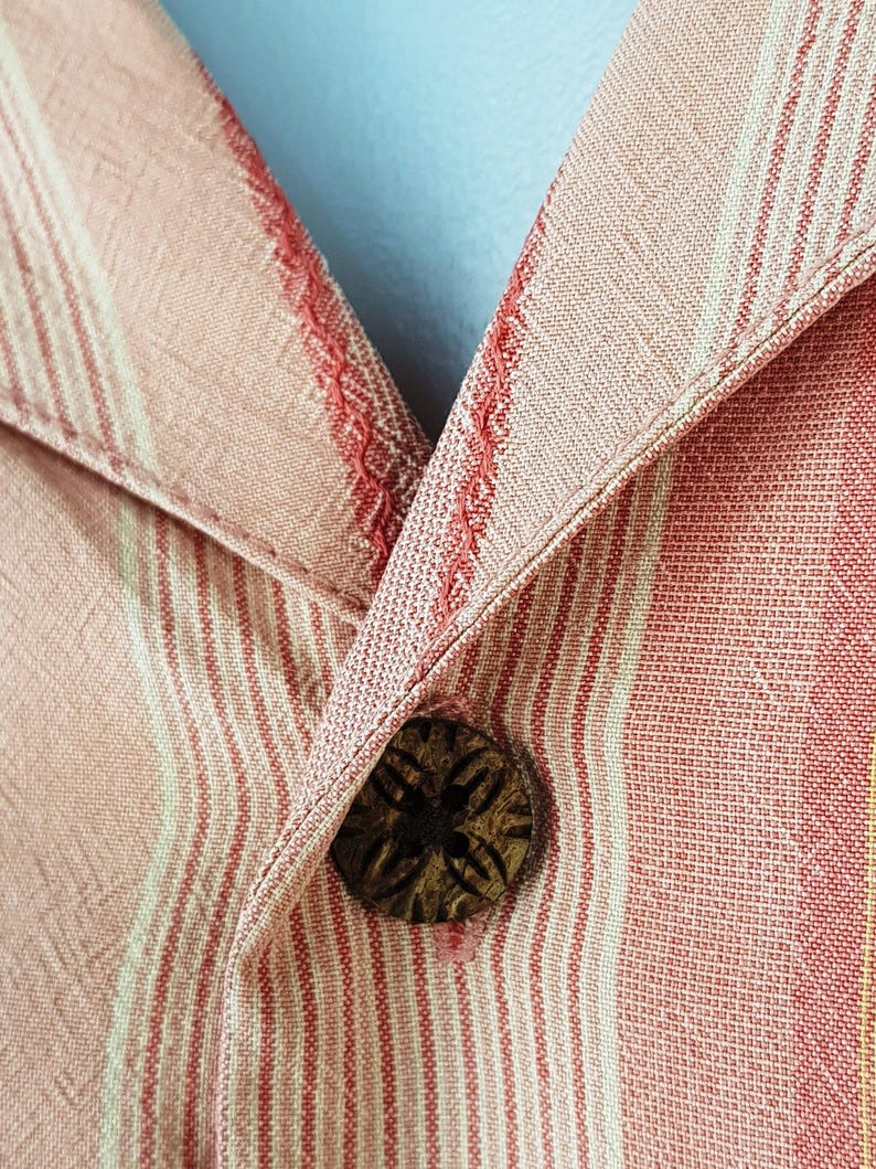 May include: Close-up of a red and white striped shirt with a wooden button. The button has a carved design.