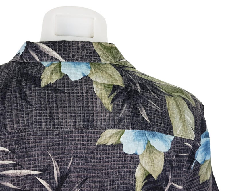 K&ouml;nnte beinhalten: Ein dunkelgraues Hemd mit Kn&ouml;pfen und einem tropischen Muster mit gr&uuml;nen Bl&auml;ttern und blauen Bl&uuml;ten.
