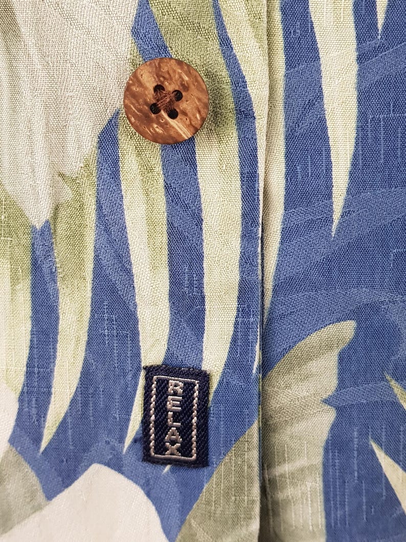 Puede incluir: Primer plano de una camisa de patr&oacute;n azul claro y verde con un bot&oacute;n de madera y una etiqueta negra que dice "RELAX".