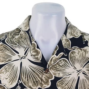 Peut inclure: Une chemise noire &agrave; boutons avec un grand motif floral dans les tons cr&egrave;me et vert olive. La chemise est pr&eacute;sent&eacute;e sur un mannequin blanc, mettant en valeur le col et les boutons. Le motif floral est pro&eacute;minent.