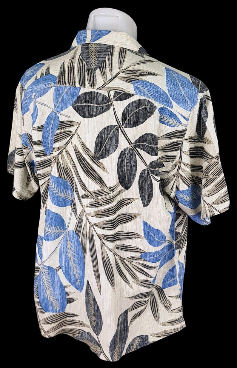 May include: A short-sleeved button-down shirt with a tropical leaf print. The shirt is white with blue and brown leaves.