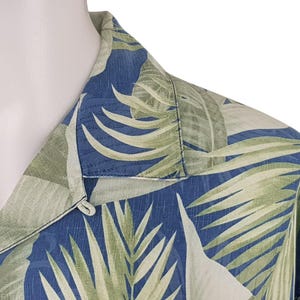 Puede incluir: Una camisa de botones azul y verde con cuello. La camisa tiene un dise&ntilde;o de hojas tropicales.