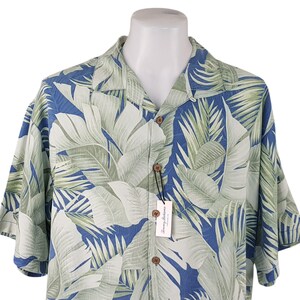 Puede incluir: Una camisa de manga corta con botones azul y verde con estampado de hojas tropicales. La camisa tiene cuello y cierre de botones. La camisa est&aacute; hecha de una tela ligera y es perfecta para el clima c&aacute;lido.