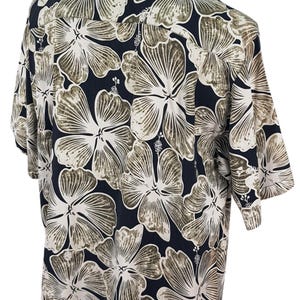 Peut inclure: Chemise &agrave; manches courtes avec un motif floral. La chemise pr&eacute;sente de grandes fleurs d'hibiscus stylis&eacute;es en blanc et marron sur un fond bleu marine fonc&eacute;. La chemise est pr&eacute;sent&eacute;e sur un mannequin.