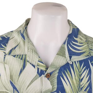 Puede incluir: Una camisa de estampado tropical azul y verde con cuello abotonado y un solo bot&oacute;n de cierre. La camisa tiene un corte holgado y est&aacute; hecha de una tela ligera.