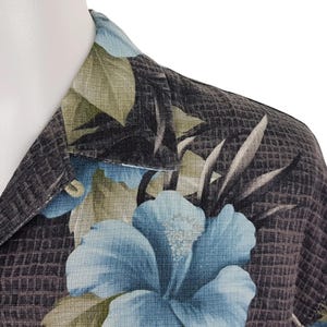 K&ouml;nnte beinhalten: Ein schwarz-blaues Hemd mit floralem Muster. Das Hemd hat einen Knopfkrag und kurze &Auml;rmel.