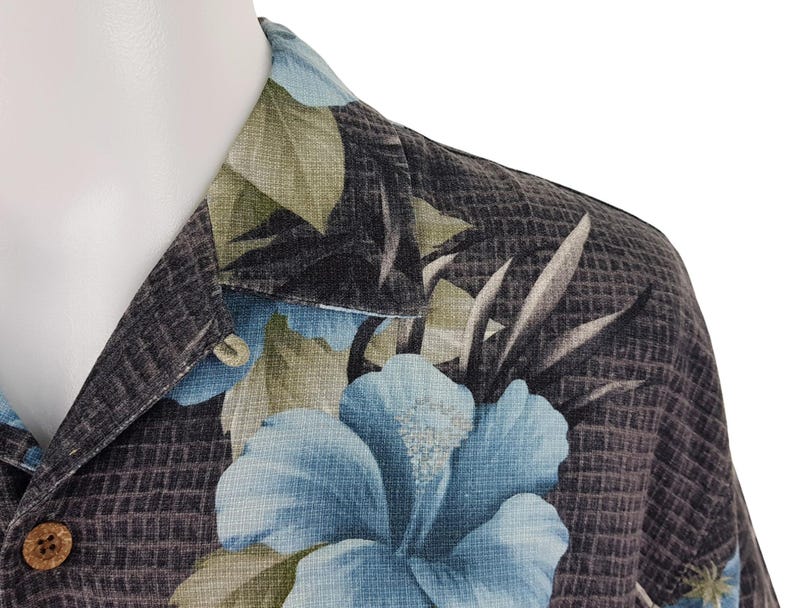 K&ouml;nnte beinhalten: Ein schwarz-blaues Hemd mit floralem Muster. Das Hemd hat einen Knopfkrag und kurze &Auml;rmel.