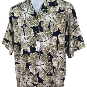 Peut inclure: Chemise &agrave; manches courtes avec un fond noir et un grand motif floral en blanc et vert olive. La chemise a un col classique et une &eacute;tiquette attach&eacute;e. Boutonn&eacute;e.