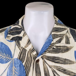 May include: A beige button-up shirt with a tropical print featuring blue, black, and brown leaves. The shirt has a collar and a button closure.