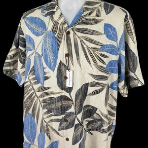 May include: A beige short-sleeved button-down shirt with a tropical leaf print in shades of blue, black, and brown. The shirt has a collar and a button closure.