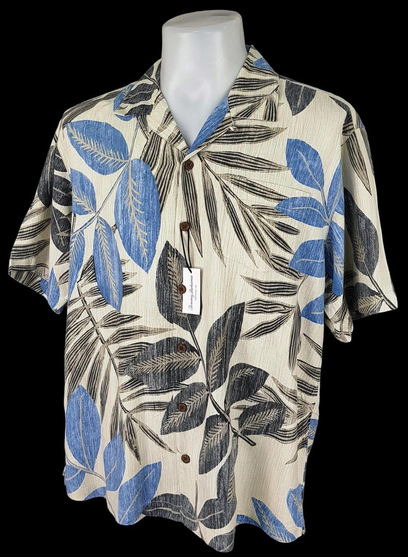 May include: A beige short-sleeved button-down shirt with a tropical leaf print in shades of blue, black, and brown. The shirt has a collar and a button closure.