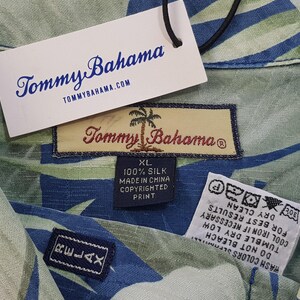 Puede incluir: Una camisa de seda con estampado verde y azul con una etiqueta de Tommy Bahama. La etiqueta dice "100% Seda, Hecho en China, Impresi&oacute;n con derechos de autor, XL".