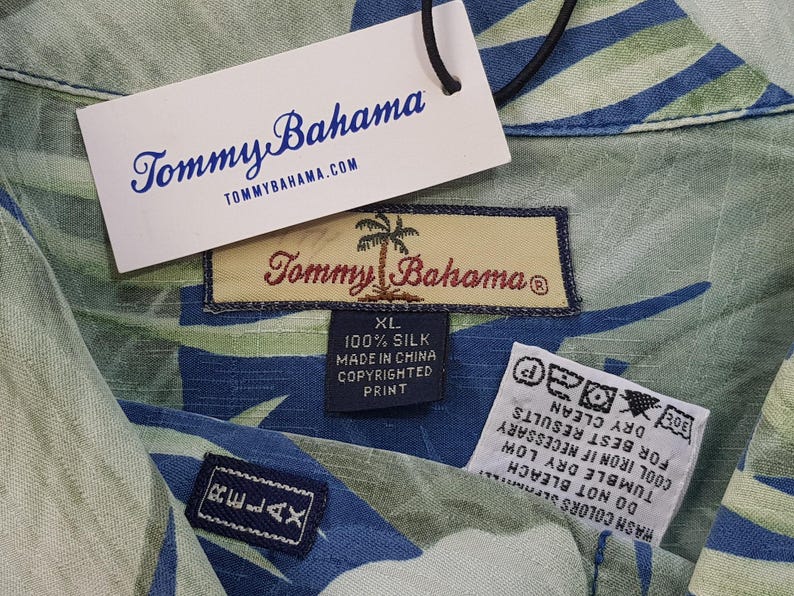 Puede incluir: Una camisa de seda con estampado verde y azul con una etiqueta de Tommy Bahama. La etiqueta dice "100% Seda, Hecho en China, Impresi&oacute;n con derechos de autor, XL".
